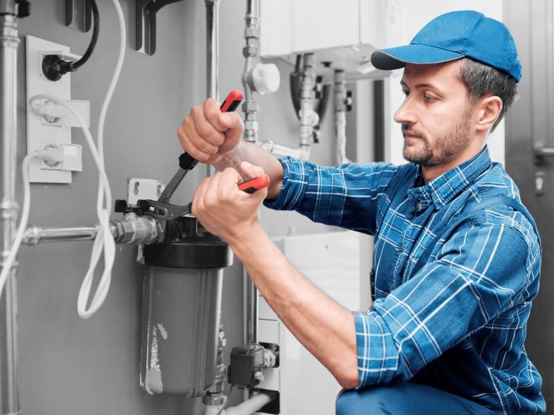 Emergency plumber in a blue hard hat repairing a burst water line with water flooding around the pipe