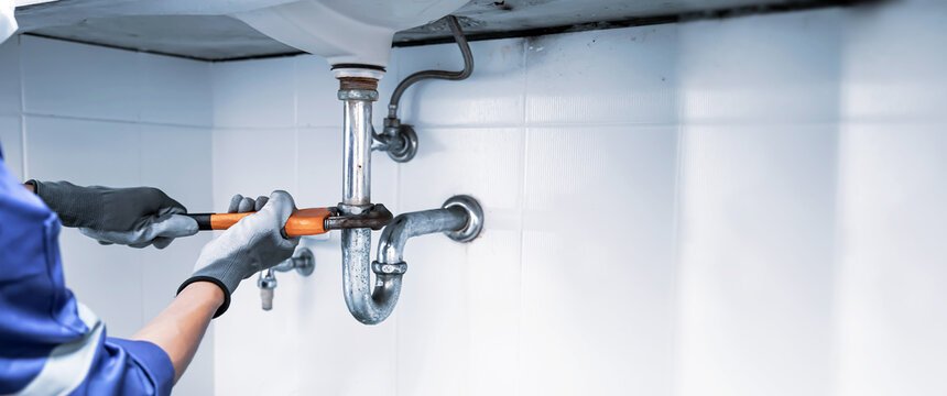 Plumber in blue coveralls holding a broken pipe as water pours onto the floor