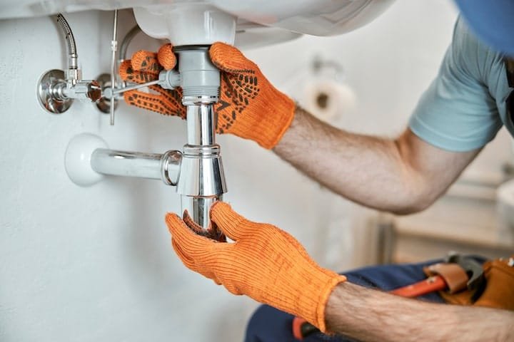 Commercial plumber in a yellow hard hat and blue overalls working on large white commercial piping
