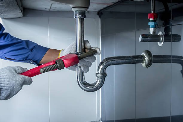 Residential plumber in a plaid shirt and overalls repairing a faucet valve above a white sink